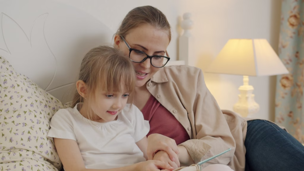 Mother and daughter reading a book together in bed in warm lamplight, a calm and connected bedtime moment