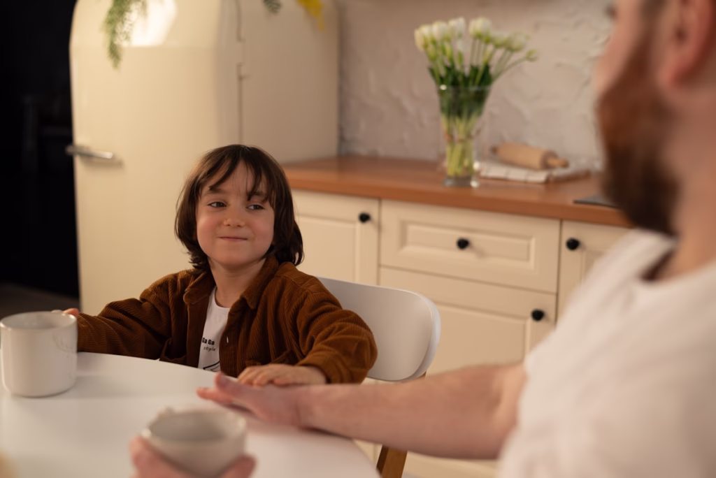 Parent leaning in attentively while child speaks at a table, warm indoor light, a moment of genuine listening and connection